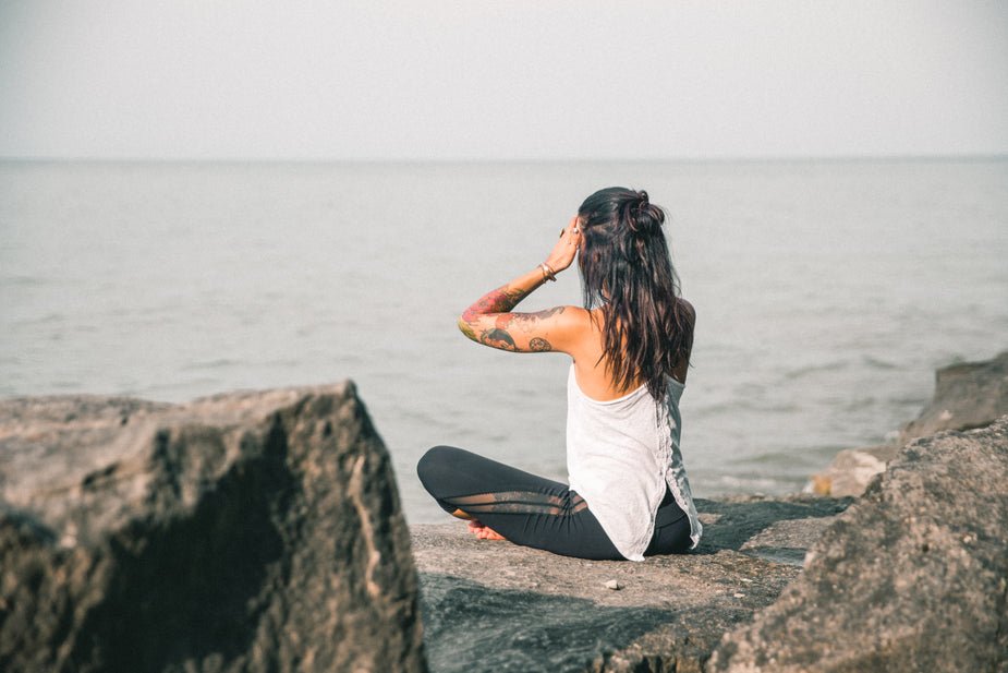 Woman meditating cross-legged on a rock overlooking the ocean at sunrise
